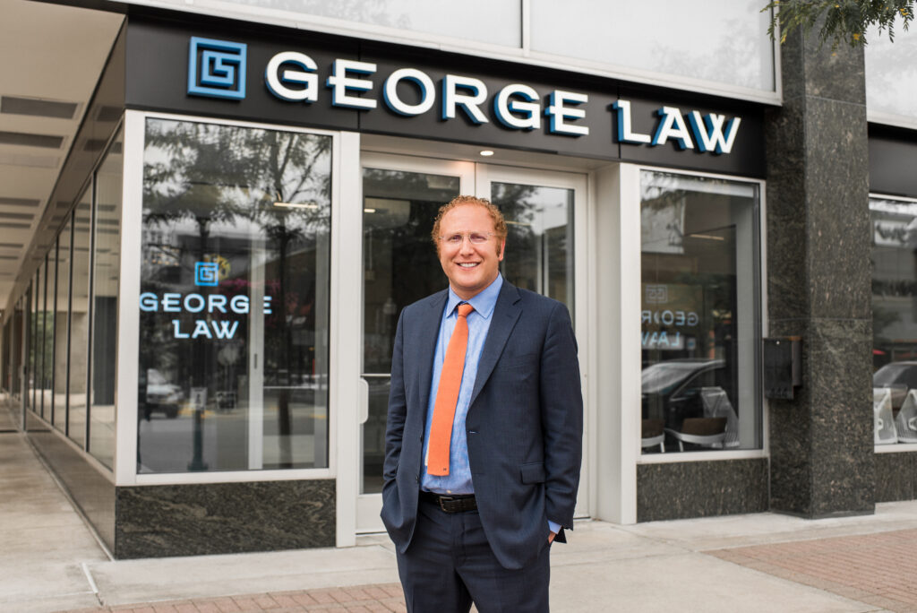 Criminal defense and DUI lawyer Derrick George in a navy blue suit in front of his law firm with signage that says George Law