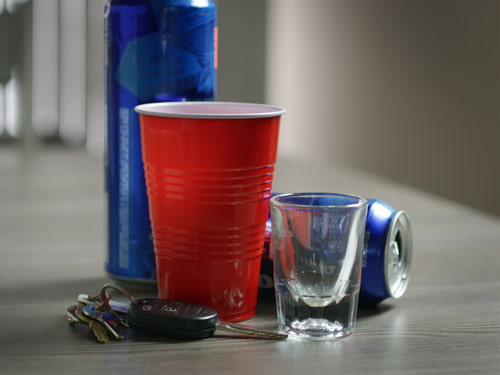 Open alcohol containers and a shot glass next to car keys on a table symbolizing the laws on open alcohol containers