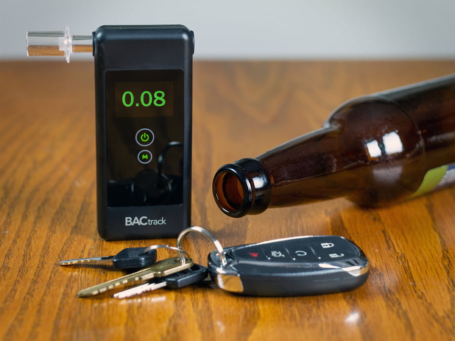 A breathalyzer device is shown with a reading of 0.08 which is the legal limit for a DUI in Michigan. The device is next to car keys and an empty beer bottle on a wooden table.