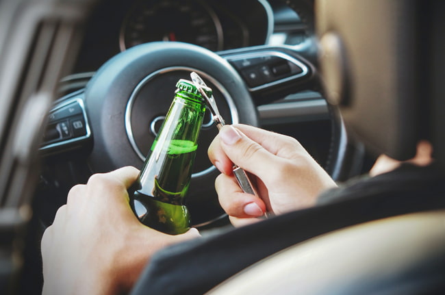 A driver is shown opening a beer while sitting in the drivers seat of a car on private property
