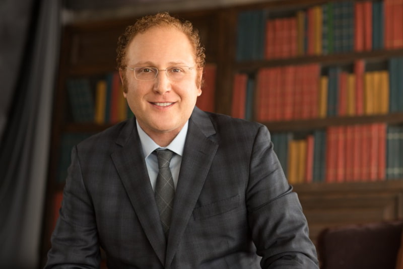 Headshot of Derrick George Attorney sitting in front of a bookshelf