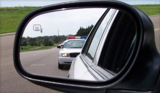 A police car is shown in a side view mirror during a traffic stop