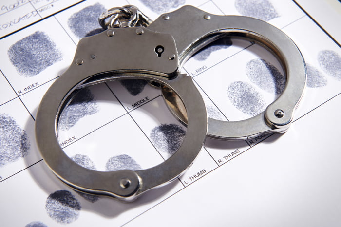 a pair of chrome handcuffs are laid on top of a paper fingerprint chart, implying the arrest arrest and fingerprinting of a suspect
