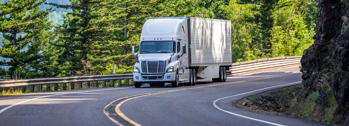 a commercial semi truck drives around a curve on a two lane blacktop road with a guardrail on one side