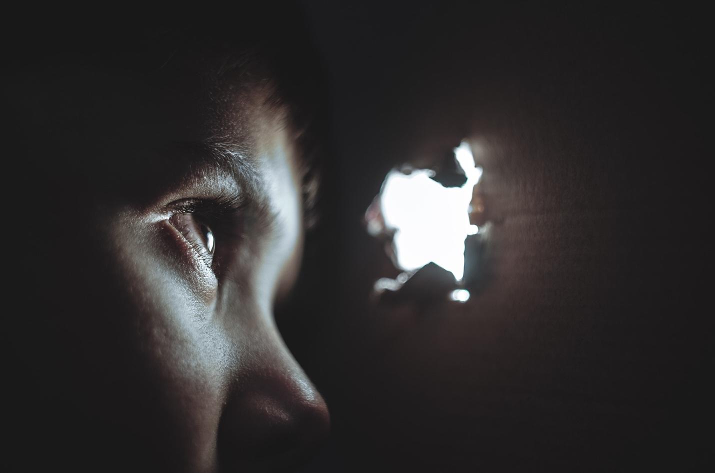 Featured: Person's face looking through a peephole on black background- Michigan Voyeurism Lawyer - MCL 750.539
