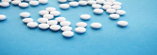 Featured: White prescription pills on blue table- Michigan Prescription Drug Charge Lawyer- George Law